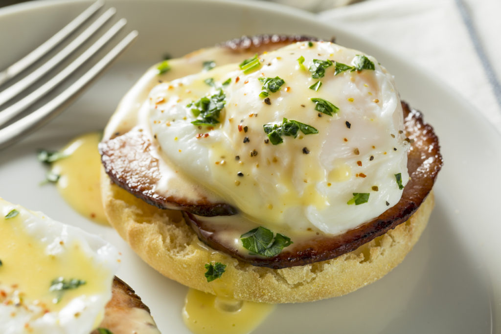 Eggs Benedict with fork on white plate